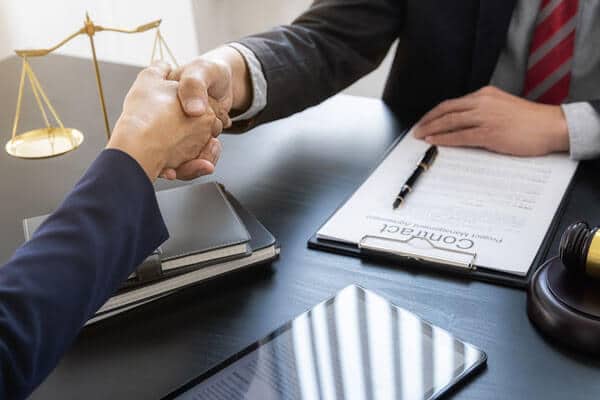 Closeup of two people shaking hands in a law office with a contract