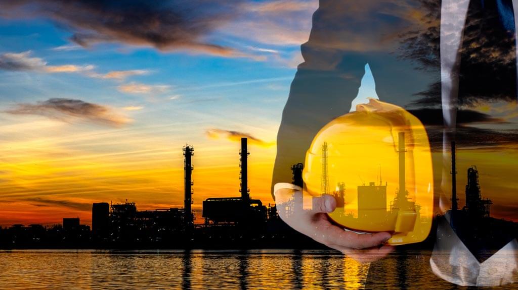 Close up of engineer holding hard hat in front of a power plant at sunset