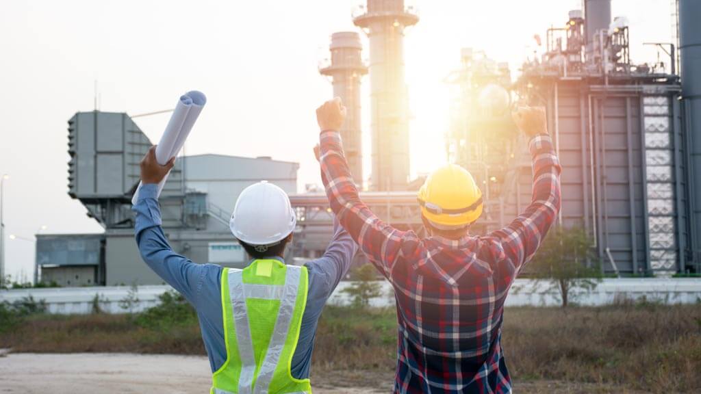 Two engineers celebrating in front of a power plant